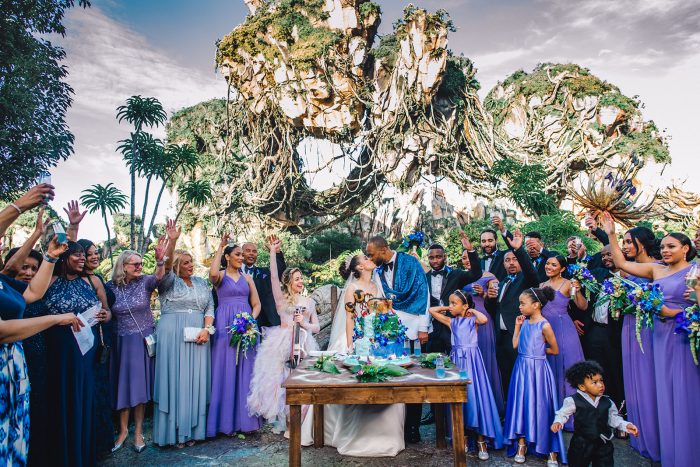 Groom Kissing Real Bride While Wedding Party Cheers by Wedding Cake