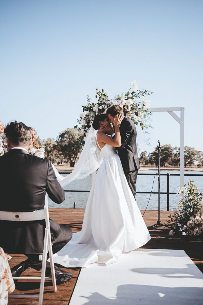 Groom Kissing Bride at Vineyard Wedding Ceremony While Bride Modern Satin Wedding Dress by Maggie Sottero