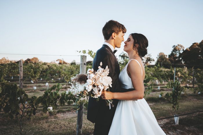 Groom Hugging Bride Wearing Maggie Sottero Wedding Dress and Holding Nude Rose Bridal Bouquet