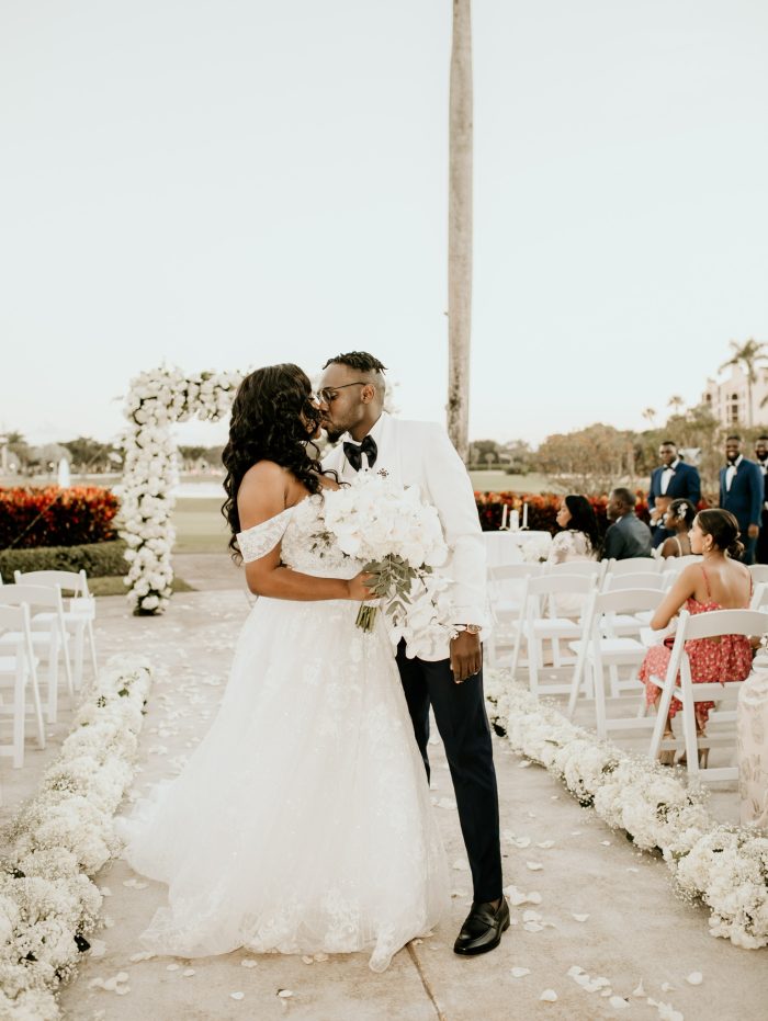 Curvy Black Bride Wearing An A-Line Wedding Dress Called Parker By Maggie Sottero Standing Under Flower Arch With Black Groom
