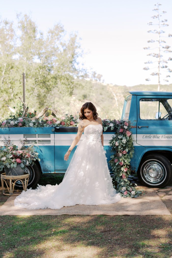 Bride wearing floral A-line wedding dress standing next to a blue truck with bright florals