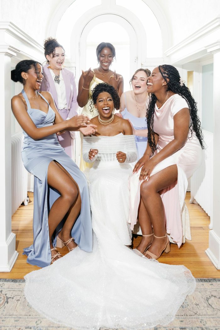 Bride wearing Drew by Maggie Sottero wedding dress laughs with her bridesmaids in pastel gowns during a joyful getting-ready moment