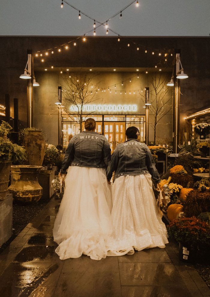Same-Sex Couple Wearing Matching Denim Jackets That Say Wifey While Wearing Maggie Sottero Wedding Dress