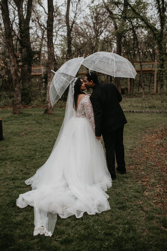 Black Bride Standing With Husband Under Clear Umbrellas Wearing An A-Line Lacy Wedding Gown Called Mallory Dawn By Maggie Sottero