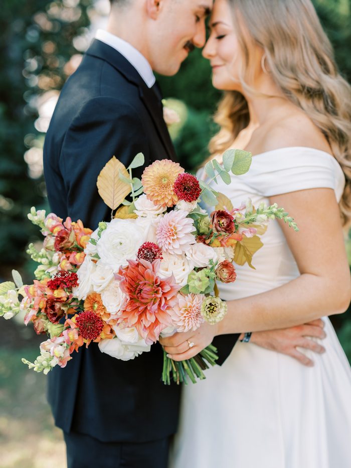 Bride wearing Ekaterina wedding gown by Maggie Sottero and holding a Peach Fuzz colored bouquet.