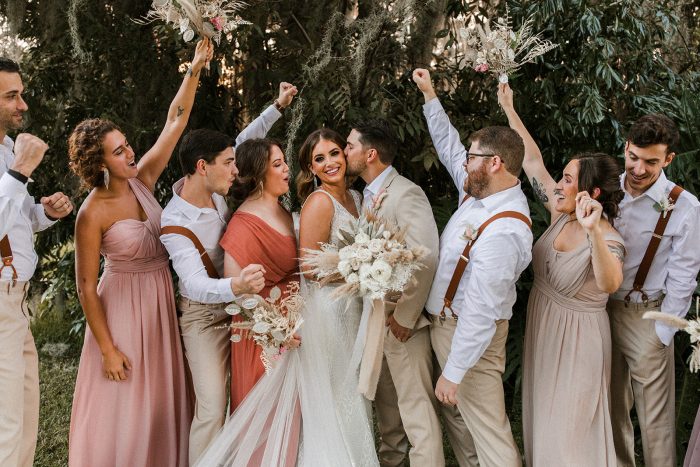 Real Bride and Groom Kissing at Outdoor Wedding with Bridal Party Cheering on the Side