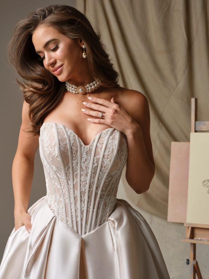Close-up of Ashland's strapless lace corset bodice with exposed boning on a satin ballgown wedding dress, paired with layered pearl jewelry and soft glam bridal makeup.