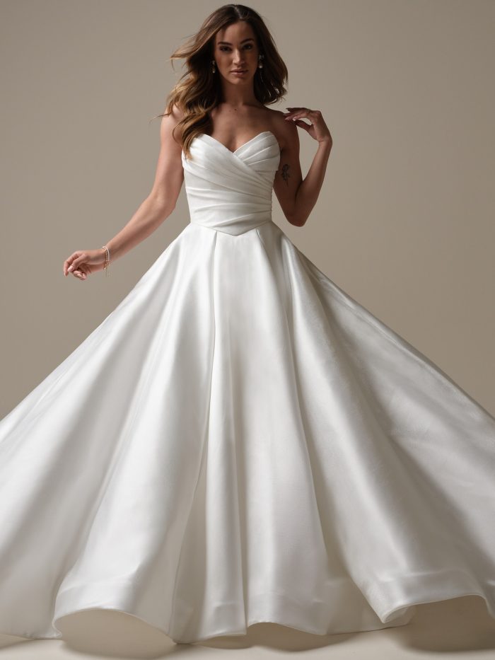 Bride wearing a strapless satin ball gown wedding dress with a ruched bodice and sweetheart neckline, twirling gracefully in soft studio lighting.