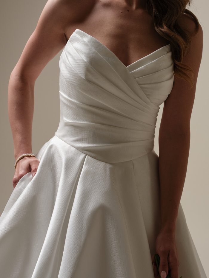 Close-up of a strapless satin ball gown wedding dress featuring a ruched bodice and sweetheart neckline, highlighting the smooth texture and elegant pleating detail.