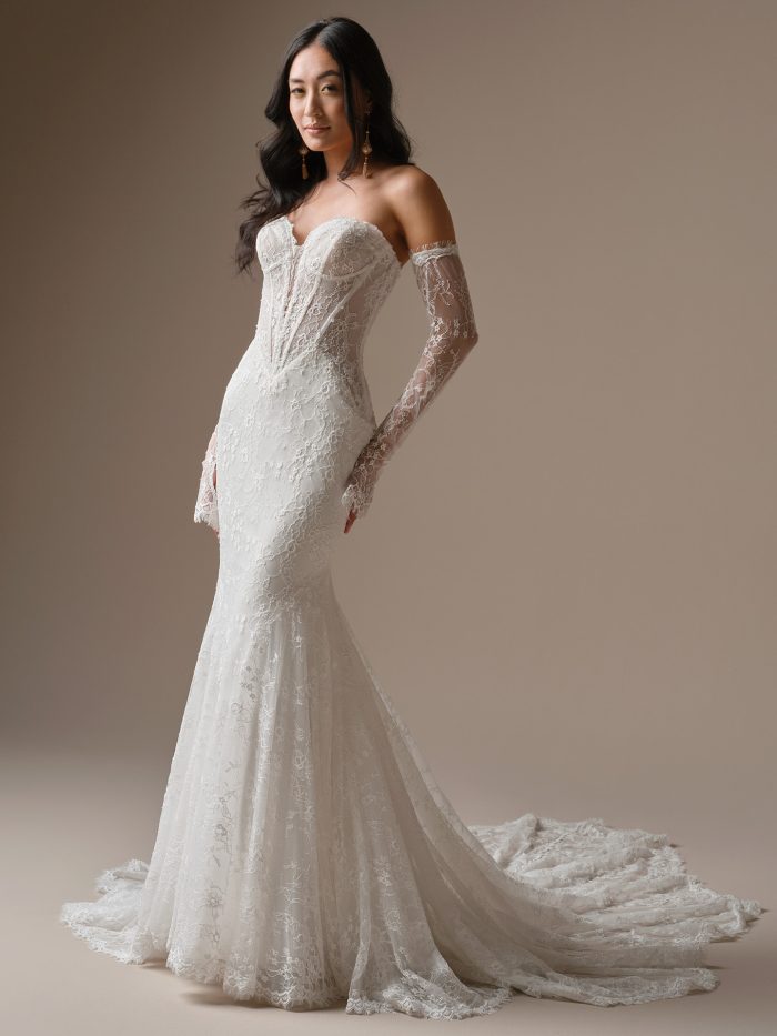 Bride wearing Bellevue by Maggie Sottero, a strapless fit-and-flare lace wedding dress with exposed boning, sweetheart neckline, and detachable illusion lace sleeves, shown in ivory.