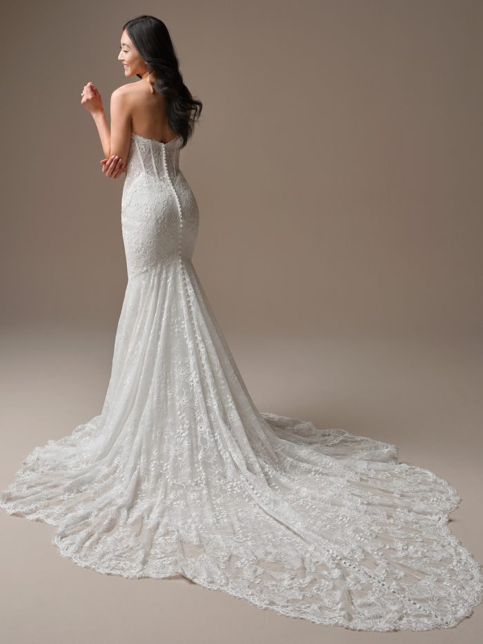 Back view of Bellevue by Maggie Sottero, a strapless lace fit-and-flare bridal gown with corset-style bodice, covered buttons, and a dramatic lace train.