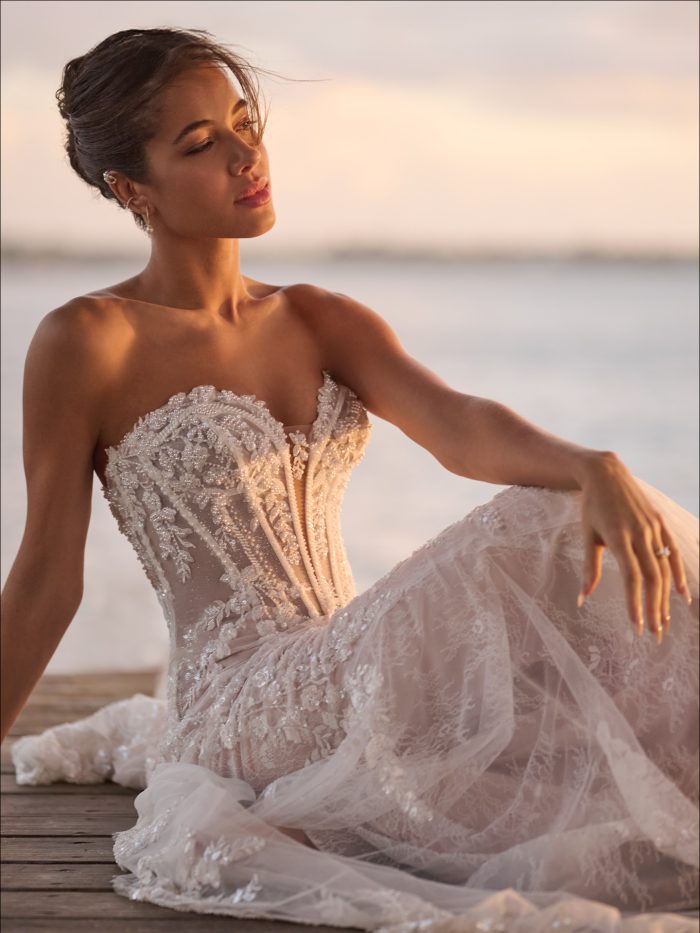 Close-up of the Benjie Royale by Maggie Sottero strapless fit-and-flare wedding dress featuring a sheer corset bodice with intricate lace appliqués and a flowing lace skirt by the water.