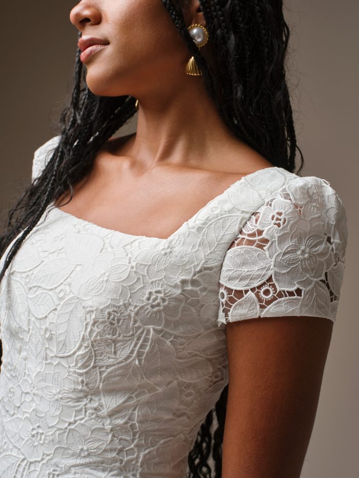 Close-up of Dakota Leigh by Maggie Sottero, unembellished floral lace bodice with modest square neckline and short cap sleeves, classic sheath bridal gown.