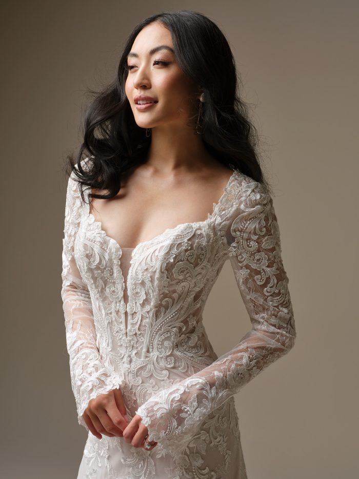 Close-up view of the Farrah wedding dress showing the plunging illusion V neckline, illusion lace bodice with exposed boning detail, sequin lace motifs over Chantilly lace, and Chantilly lace covered buttons trailing down the back.