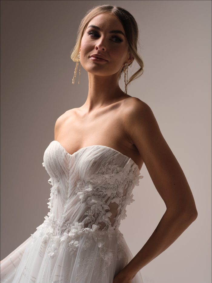 Close-up of the Ireland wedding dress by Maggie Sottero, highlighting the strapless sweetheart neckline, sheer pleated bodice with 3-D floral beaded lace, and delicate glitter tulle detailing for a celestial, boho look.
