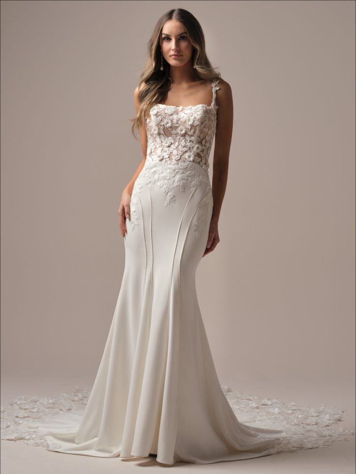 Bride wearing the Isoline fit-and-flare wedding dress featuring a crepe sheath silhouette, square neckline, floral lace illusion bodice, and a sleek skirt with a soft lace-trimmed train, photographed in a studio setting.