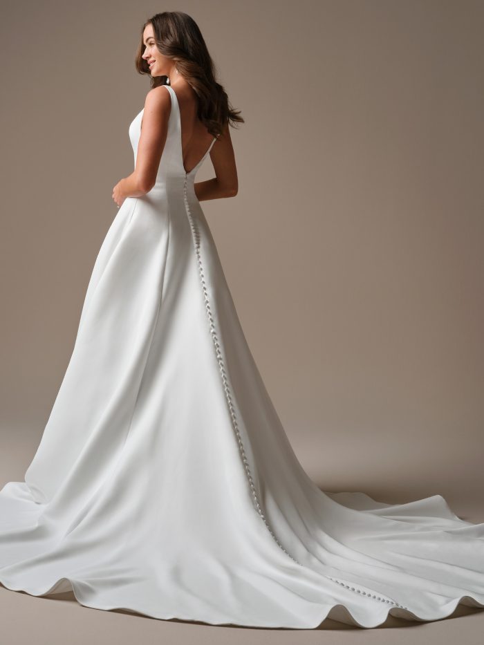 Back view of the Lawrence A-line wedding dress showing the deep V-back, satin-covered buttons trailing down the train, and the gown’s smooth, sculptural silhouette.