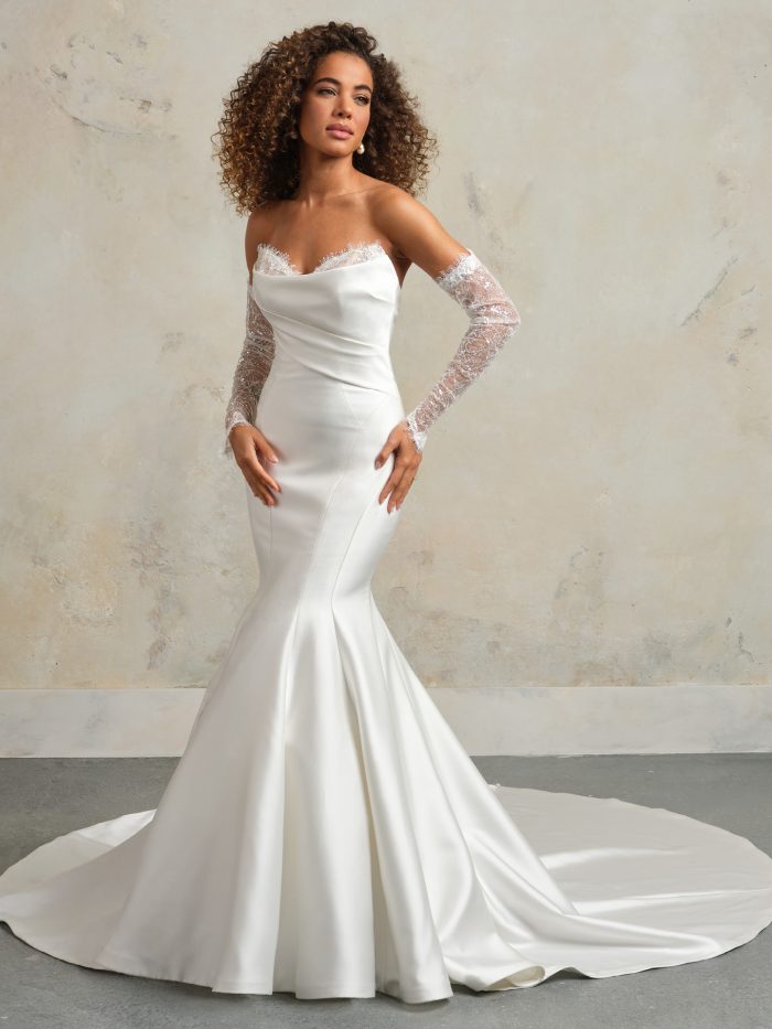 Bride wearing strapless fit-and-flare satin wedding dress with delicate lace trim along the neckline, detachable lace sleeves, and sleek silhouette with chapel-length train.
