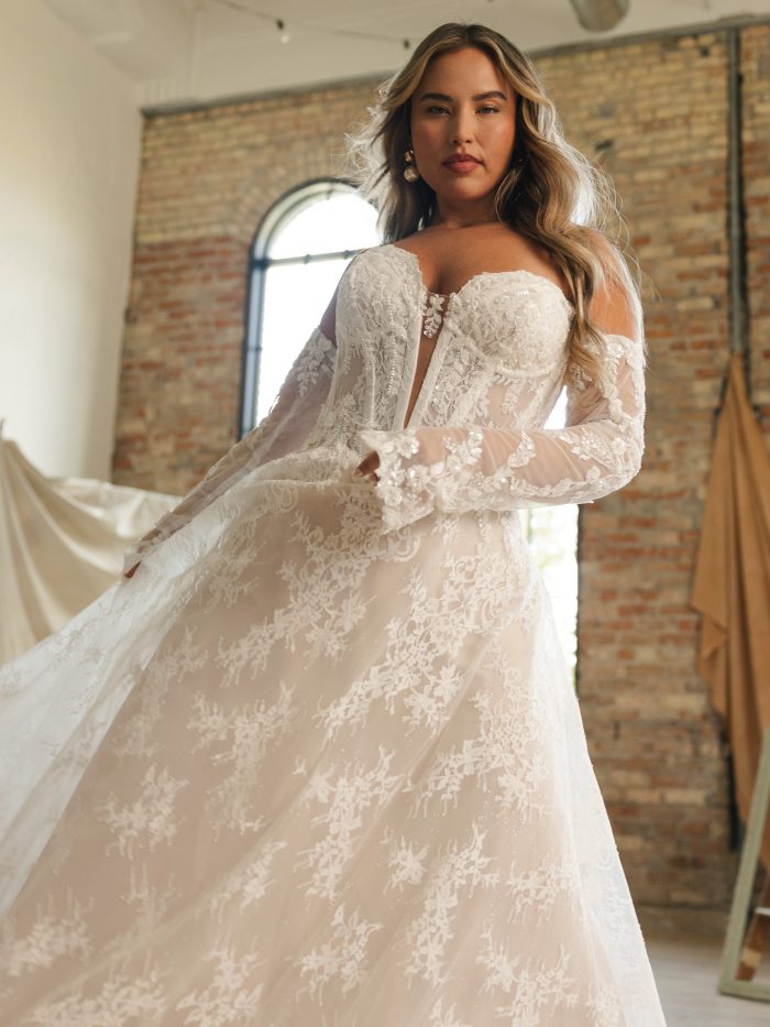 Bride wearing Lucca by Maggie Sottero, a romantic A-line lace wedding dress featuring a beaded illusion bodice, off-the-shoulder long sleeves, and flowing tulle skirt.