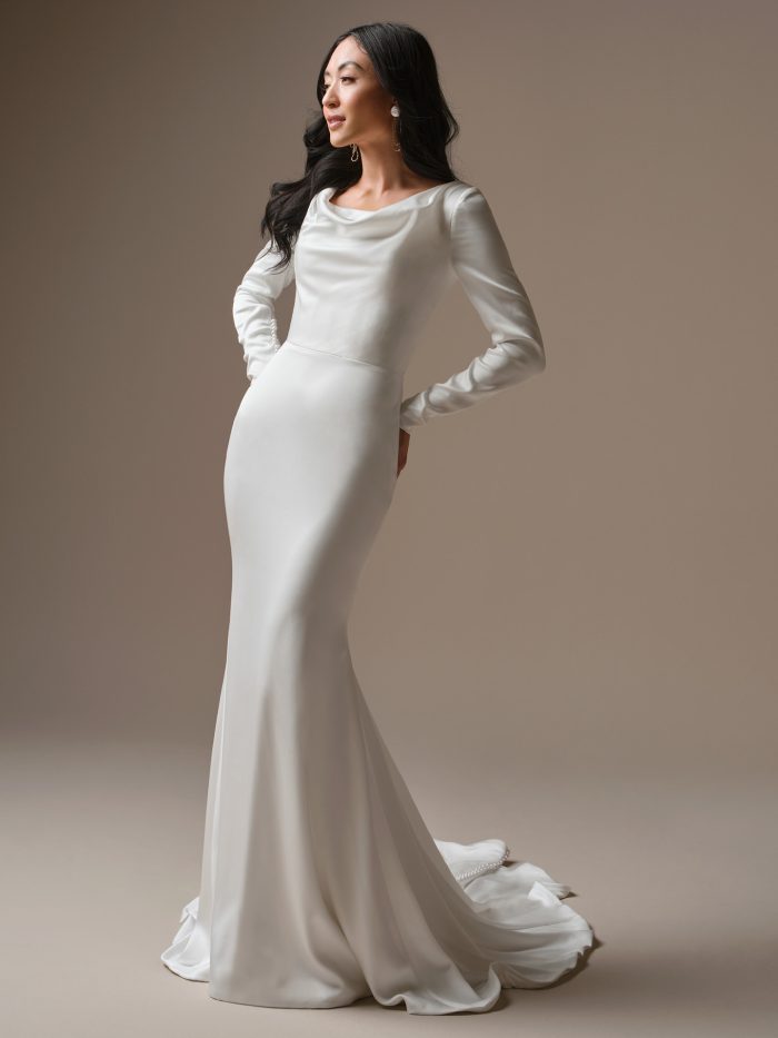 Model wearing the Melinda sheath wedding dress, featuring a soft cowl neckline, long fitted sleeves, and a sleek satin silhouette that drapes elegantly into a minimalist train.