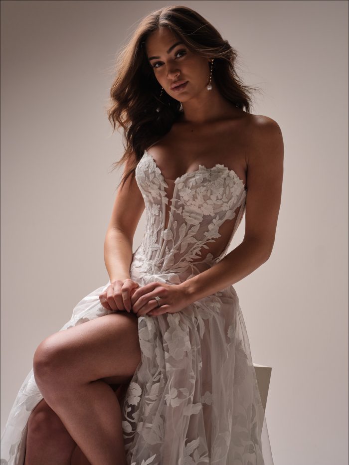 Close up of the Natalie wedding dress highlighting the plunging lace bodice, illusion side details, and soft floral tulle as the bride sits gracefully.