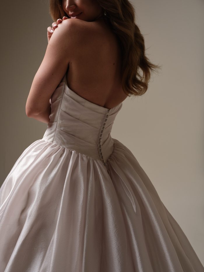Back view of a strapless satin ball gown wedding dress with covered button closure and full gathered skirt, highlighting the smooth sheen of the fabric.