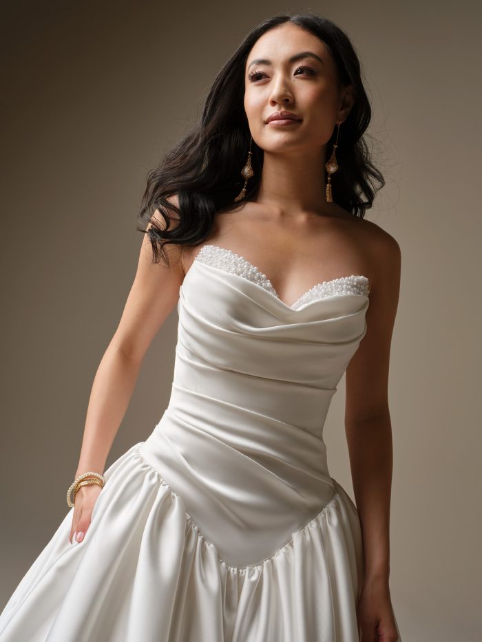 A close-up of the Maggie Sottero Pasadena wedding dress showing the draped satin bodice, pearl-accented sweetheart neckline and exaggerated basque waistline.