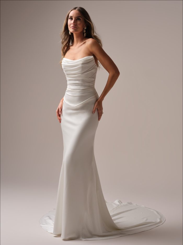 Bride wearing the Rhoda sheath wedding dress featuring a strapless draped bodice with delicate beaded trim and a sleek fitted skirt with a soft train.