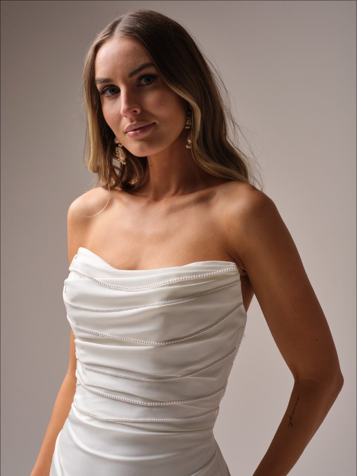 Close up of the Rhoda gown’s strapless draped bodice showcasing the beaded trim detail and smooth satin finish.