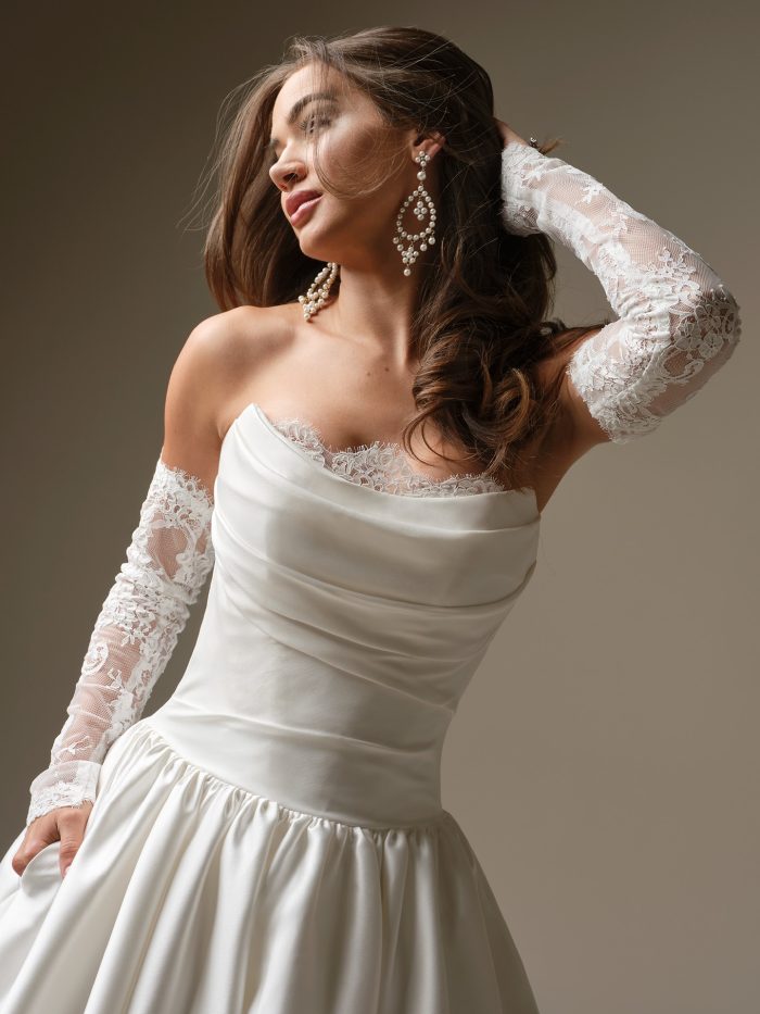 Close-up of the Maggie Sottero Sylvana wedding dress showcasing the strapless draped satin bodice, delicate lace trim at the neckline, and detachable sheer lace sleeves.