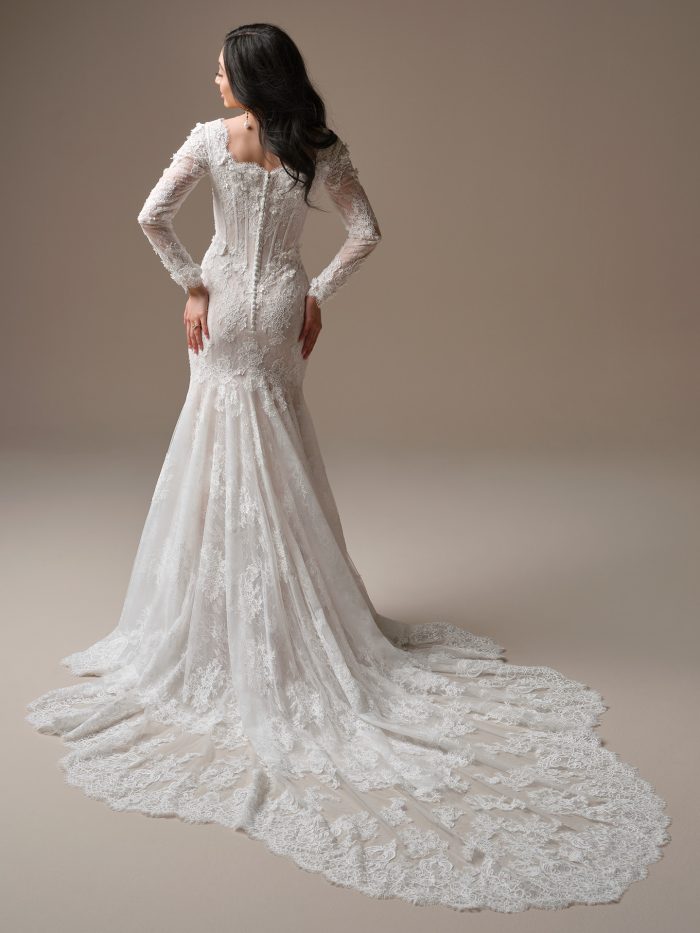 Back view of the Takera Leigh wedding dress showing the modest V-back, illusion lace sleeves with beaded 3D florals, exposed boning along the bodice, covered buttons over the zipper closure, and a full extended scalloped illusion lace train.