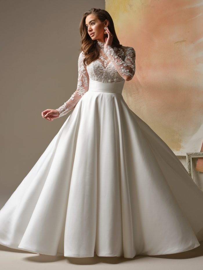 Trinity by Maggie Sottero, vintage-inspired A-line Mikado wedding dress with illusion lace bodice, mock lace turtleneck, long fitted lace sleeves, empire waist, and full skirt with pockets.