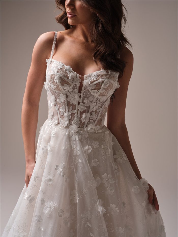 Close-up of the Wallis wedding dress highlighting the illusion bodice with dimensional floral lace appliqués, delicate beaded straps, and light-catching sparkle woven throughout the fabric.