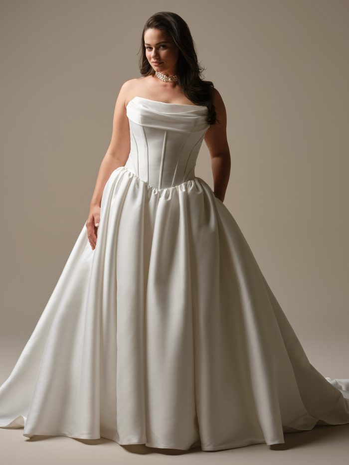 Yuma by Maggie Sottero strapless ball gown wedding dress in Felicity Mikado featuring a draped cowl neckline, basque waistline with boning, and full skirt with pockets
