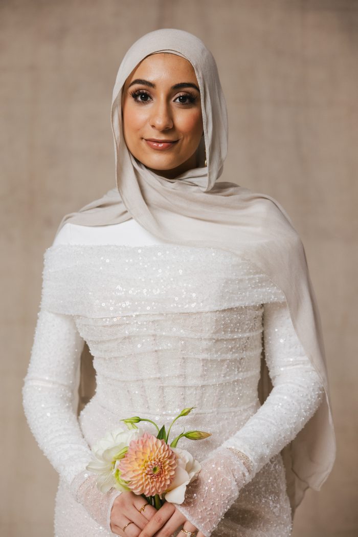 Bride wearing a headscarf in a sequin wedding dress with off-the-shoulder bridal jacket and exposed boning