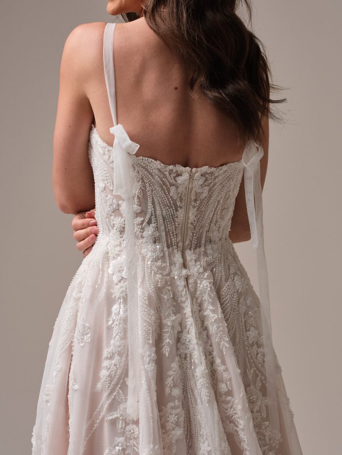Back detail of the Rebecca Ingram Angie A-line wedding dress showcasing a sheer beaded lace bodice, thin straps with soft tulle ties, and flowing tulle skirt.