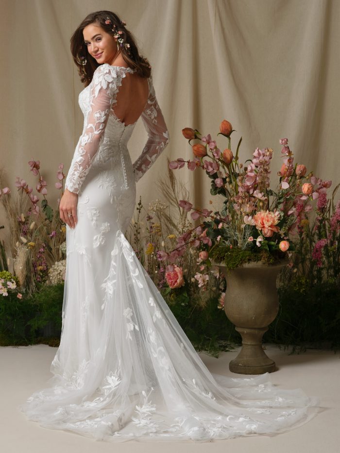 Back view of the Aubra wedding dress by Rebecca Ingram showcasing a sexy open keyhole back, illusion lace long sleeves, covered buttons, and a flowing lace train.