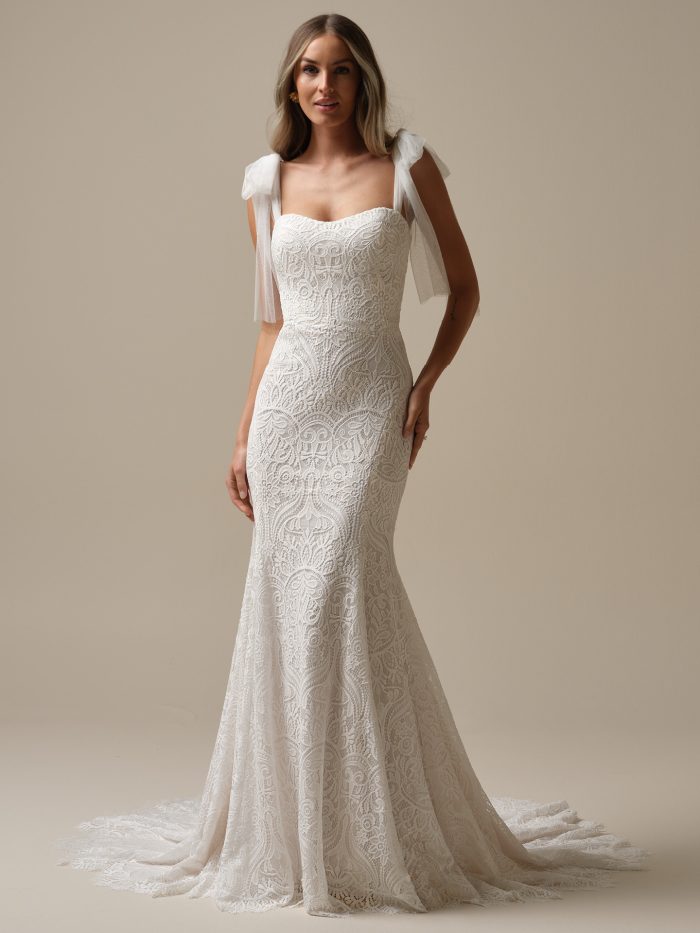 Model wearing the Rebecca Ingram Berkeley sheath wedding dress featuring allover unembellished lace, a strapless sweetheart neckline, and a scalloped lace hem.