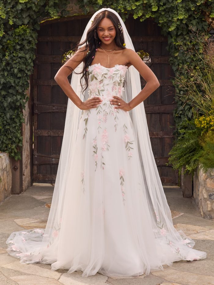 Bride wearing the Blossom A-line wedding dress featuring a strapless neckline, ethereal tulle skirt, and allover 3D floral lace appliqués in soft pastel tones, photographed outdoors in a romantic garden setting.