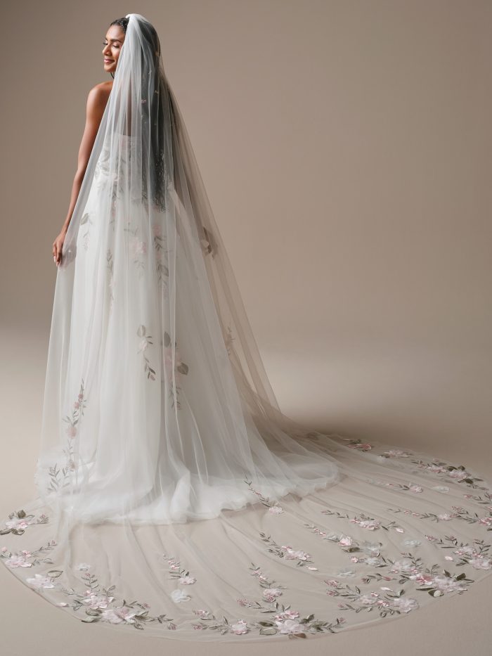 Back view of the Blossom veil by Rebecca Ingram, showcasing its flowing cathedral length and embroidered pink and green floral motifs trailing across the train.