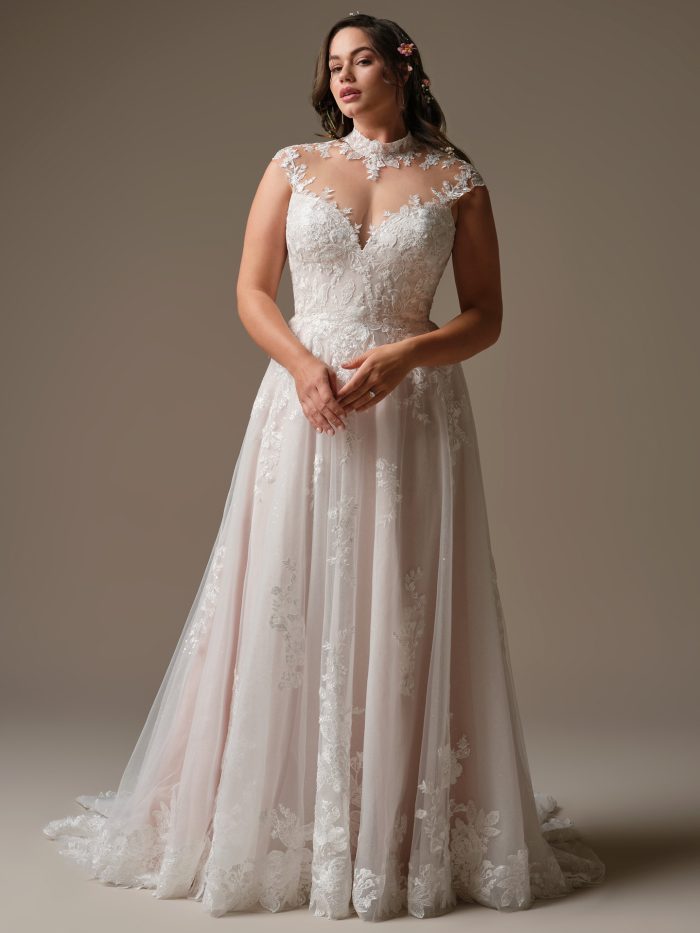 Model wearing Cody by Rebecca Ingram, an A-line wedding dress with sequined lace bodice, mock illusion turtleneck, cap sleeves, and flowing tulle skirt.