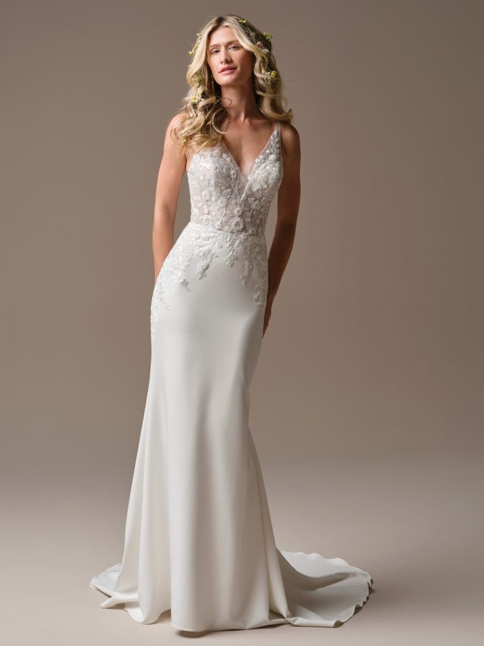 Bride wearing the Holly sheath wedding dress featuring a deep V neckline, sheer floral lace bodice, and smooth fitted skirt with subtle train detail.