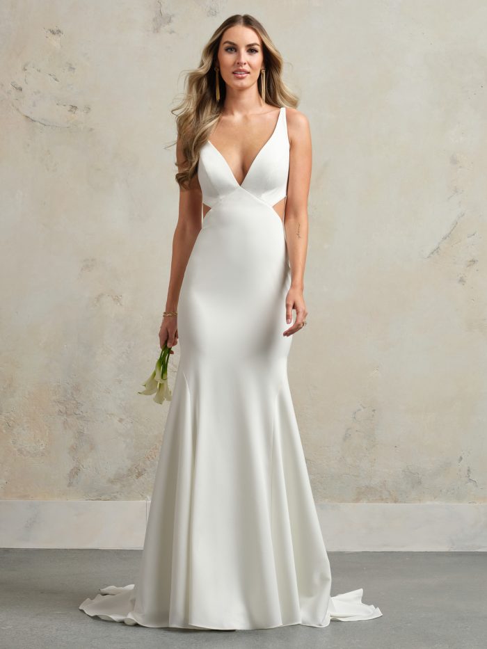 Bride wearing the Kelsey sheath wedding dress featuring a plunging V-neckline, sleek stretch crepe fabric, and subtle side cutouts, styled in a minimalist studio setting.