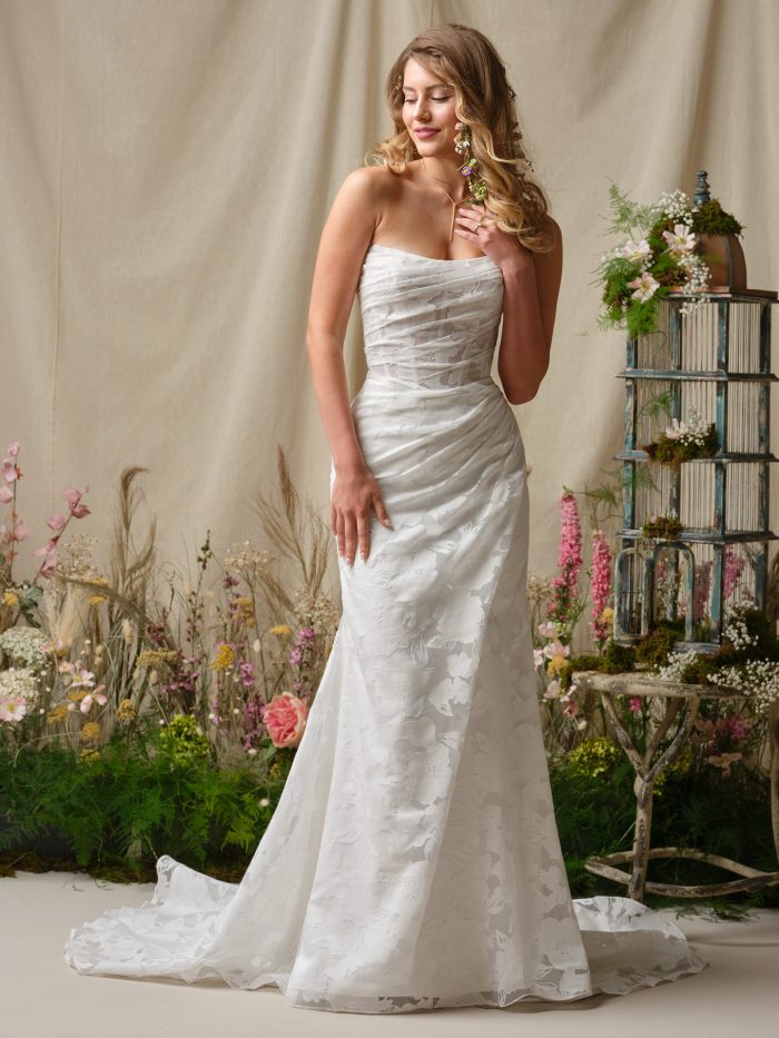 Kendall sheath wedding dress featuring printed organza, a sheer illusion bodice with exposed boning and a basque waist, and a strapless cat eye neckline.
