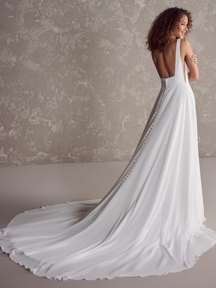 Back view of a sleeveless chiffon ball gown wedding dress featuring a deep scoop back, covered buttons, and a chapel-length train, captured in soft lighting.