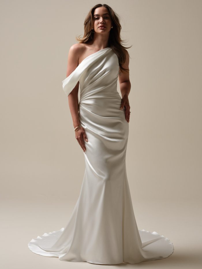 Model wearing the Rebecca Ingram Nadia sheath wedding dress featuring an asymmetrical pleated satin bodice, single-shoulder strap, and fitted silhouette.