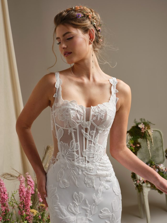 Close up of the Pearline wedding dress showing the plunging illusion square neckline, exposed boning, lace motifs, and lace tank straps.