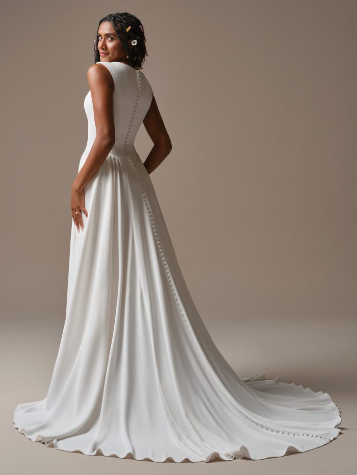 Back view of Shay by Rebecca Ingram — simple crepe A-line gown with covered buttons trailing to a soft chapel-length train.