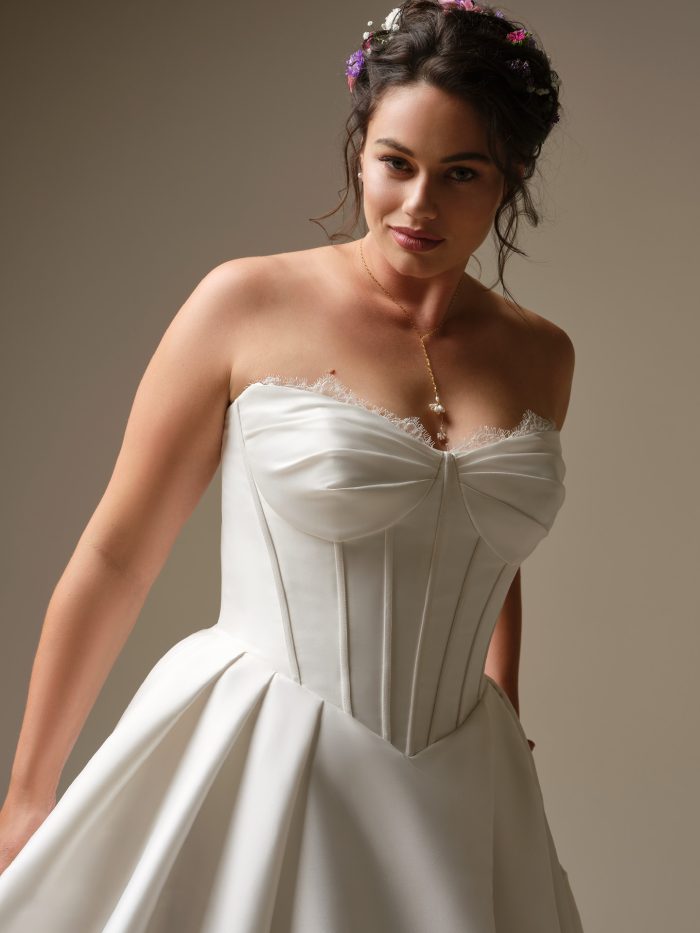 Close-up of the Rebecca Ingram Zorina wedding dress highlighting the strapless bodice with exposed boning, soft pleating, and peekaboo lace trim at the neckline.