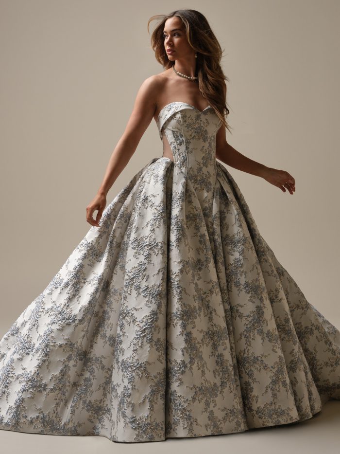 Model wearing the Aberdeen by Sottero and Midgley strapless ballgown wedding dress with a structured corset bodice, sweetheart neckline, and full skirt in floral jacquard fabric.